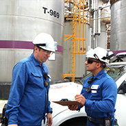 Two male workers talking over a clipboard outside at a plant.