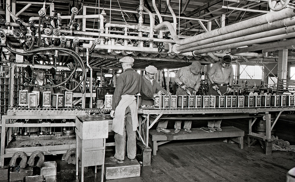 Black and white historical image of workers filling Oronite product cans at bottle plant. 