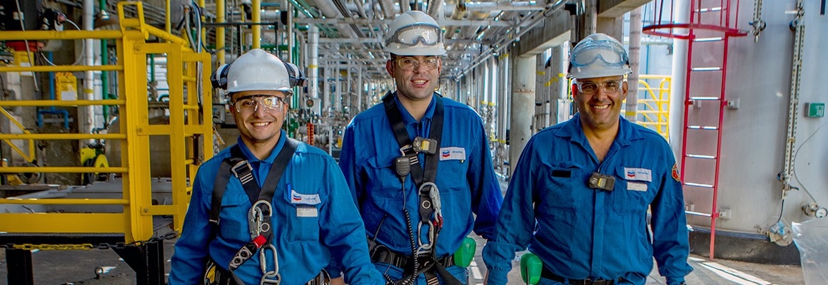 Three male workers walking towards camera at Oronite plant and smiling.