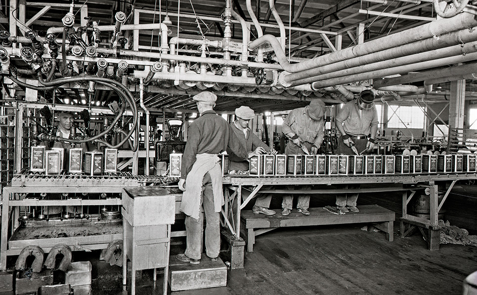 Black and white historical image of workers filling Oronite product cans at bottle plant.