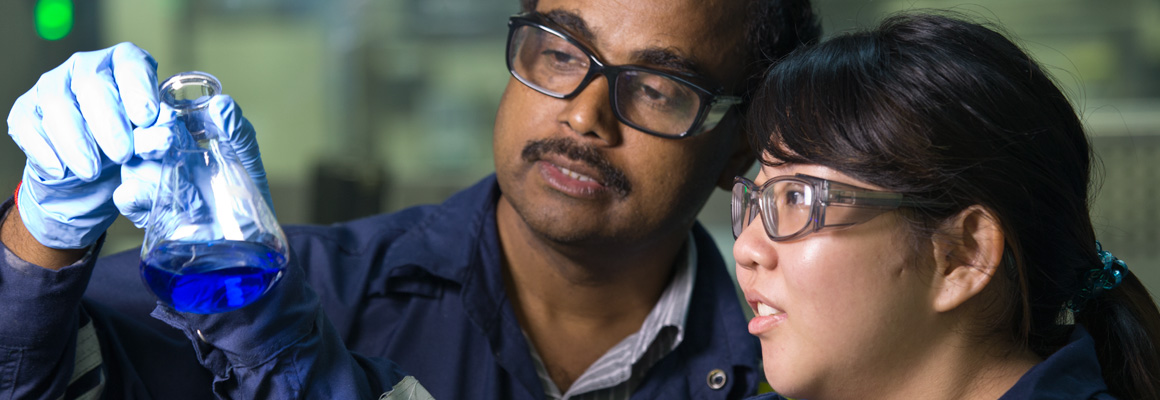 Two people holding up and looking at a beaker of chemicals in a laboratory.