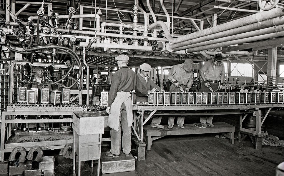 Black and white historical image of workers filling Oronite product cans at bottle plant.