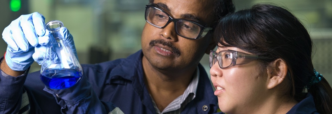 Two people holding up and looking at a beaker of chemicals in a laboratory.